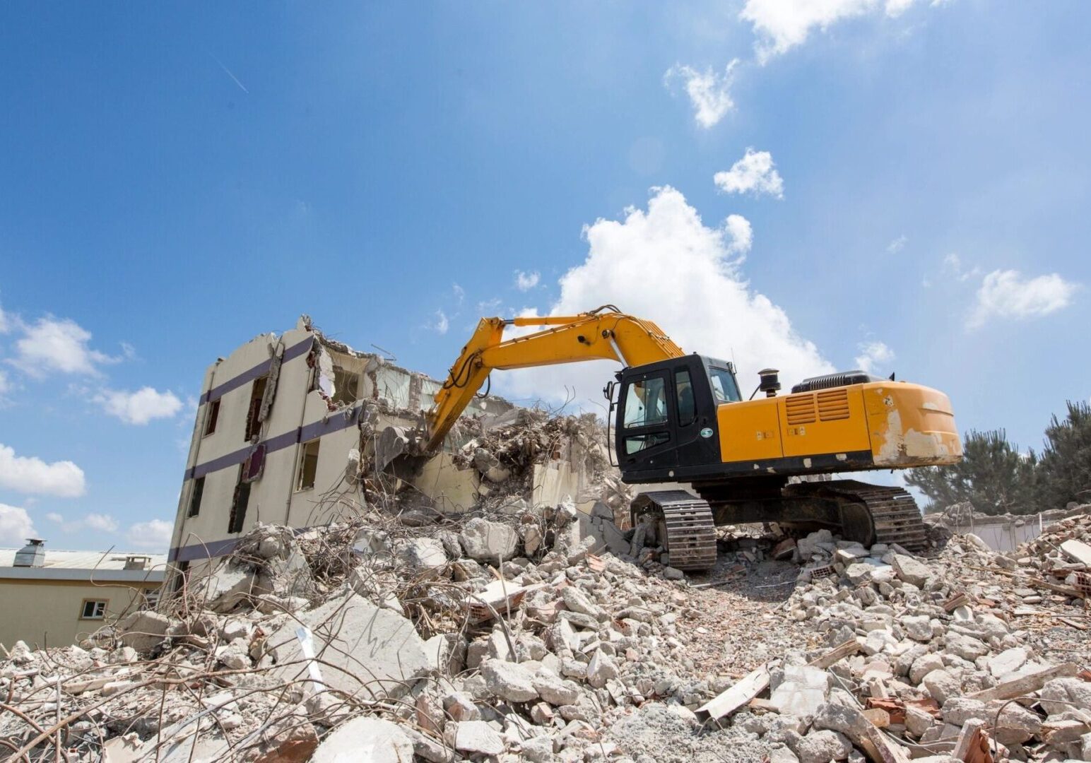 A yellow and black excavator on top of rubble.