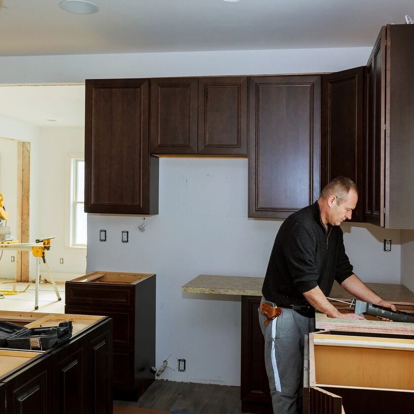 A man in black shirt standing next to brown wooden cabinets.